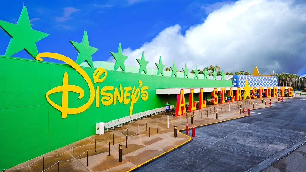 Bright Green and Yellow Disneys All-star Sports Resort Entrance with Large Stars on Top, Red and Orange All Star Sports Lettering, a Blue Sky, and Clouds in the Background. - Favorite Grampy Travels - Favorite Grampy Travels 2026