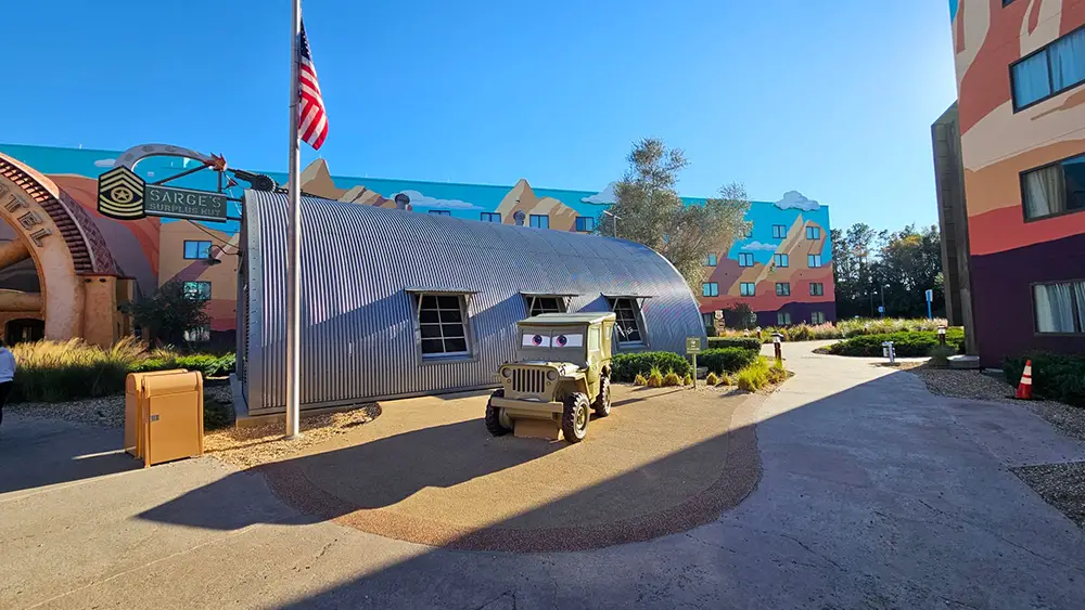 Wdw-art-of-animation-cars-courtyard - Favorite Grampy Travels a Small Army Jeep and Quonset Hut Sit Under an American Flag in a Courtyard with Colorful Cartoon-themed Hotel Buildings and Landscaping in the Background. - Favorite Grampy Travels - Favorite Grampy Travels 2026
