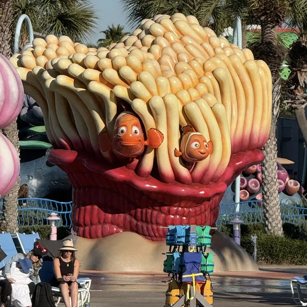 Wdw-art-of-animation-finding-nemo-pool - Favorite Grampy Travels Large Statue of Orange Clownfish in a Sea Anemone, with People Sitting Nearby in a Sunny Outdoor Area, Palm Trees, and Blue Sky in the Background. - Favorite Grampy Travels - Favorite Grampy Travels 2026