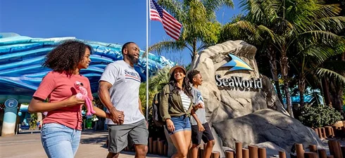 A family of four walks past the SeaWorld sign at the entrance to SeaWorld Orlando