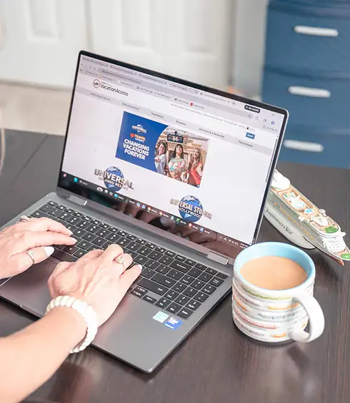 Person typing on a laptop with a website open, next to a cup of coffee and a closed book on a dark desk. A blue file cabinet and white door are in the background. - Favorite Grampy Travels