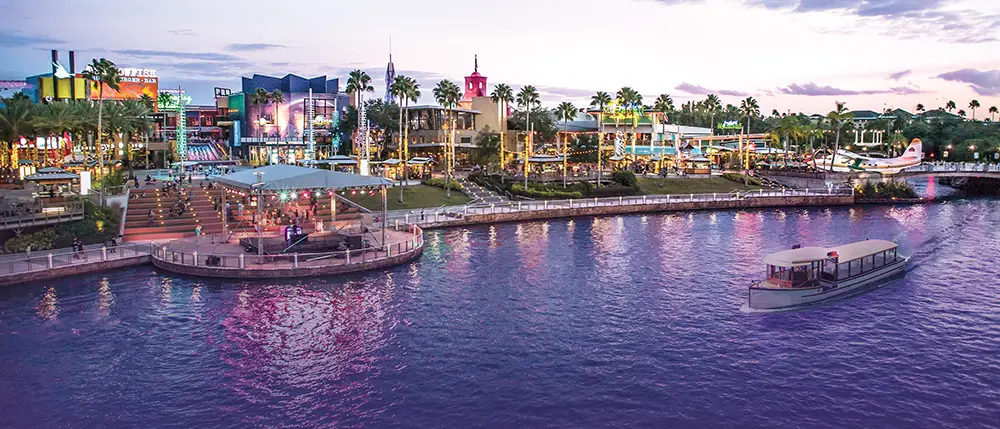 A scenic waterfront view at sunset features lively buildings, palm trees, colorful lights, and a boat gliding on the water—capturing the vibrant atmosphere of Universal CityWalk Orlando that any family guide would recommend. - Favorite Grampy Travels