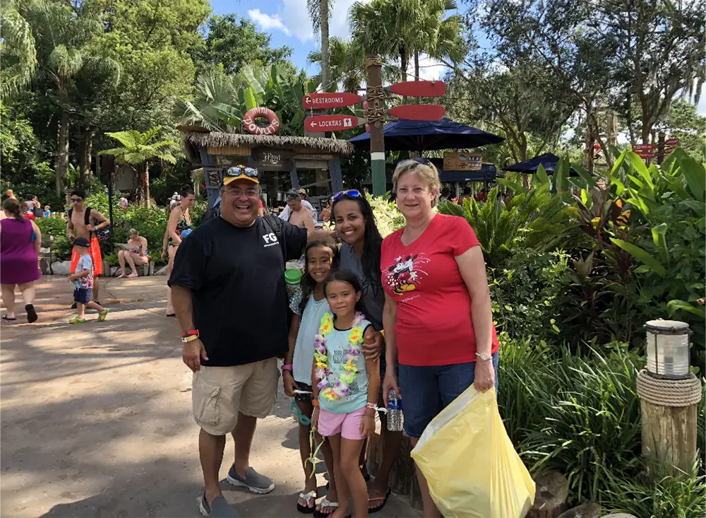 A family of four poses for a photo at a Disney World family vacation park, standing near a food stand and directional signage. - Favorite Grampy Travels