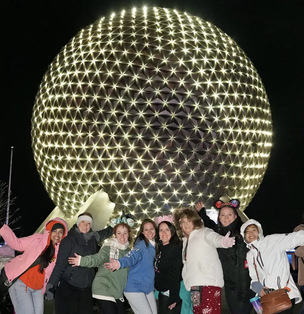 Favorite Grampy Travels advisors in winter jackets in front of Spaceship Earth at EPCOT on a quiet January night, the kind of low-crowd evening the 2027 Walt Disney World crowd calendar forecasts for mid-January - Favorite Grampy Travels