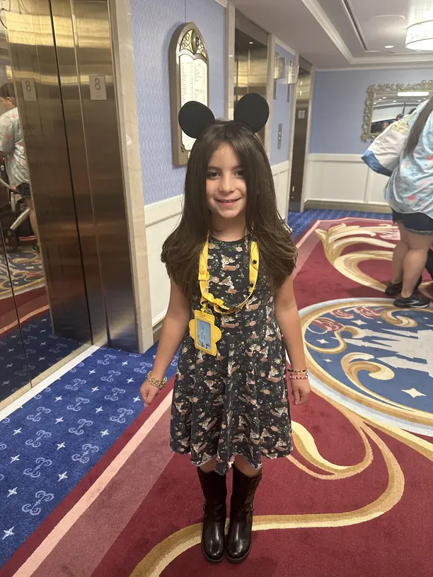 Avilene in Mickey ears with her kids club lanyard in a Disney cruise ship hallway