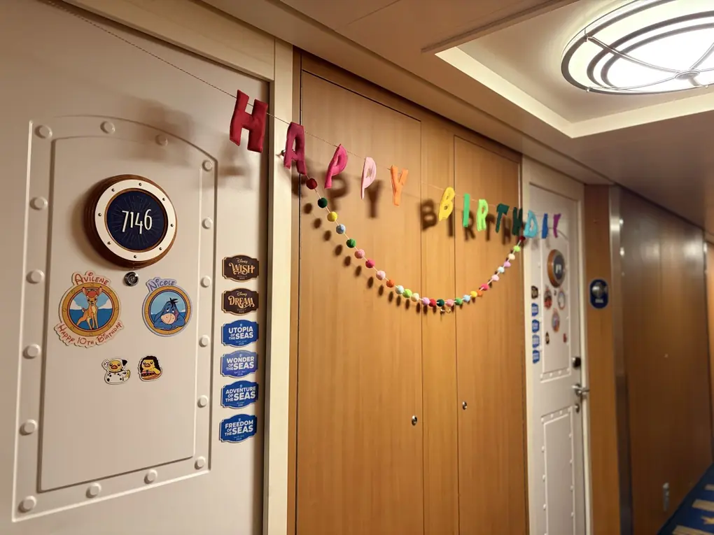 A Disney cruise stateroom door decorated with a happy birthday banner, name magnets and ship magnets