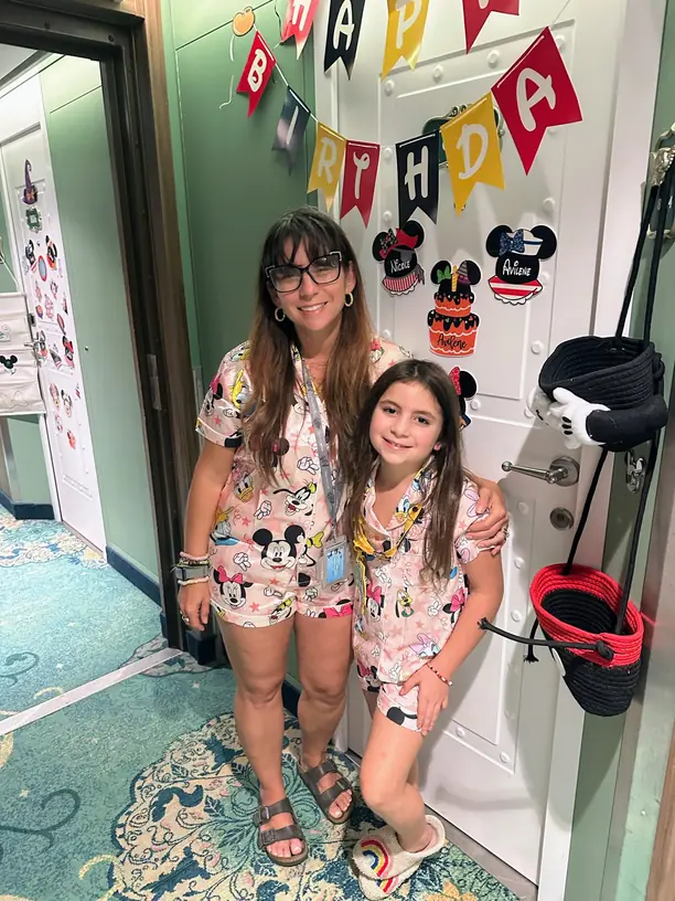 Nicole and Avilene in matching Mickey pajamas by their decorated Disney cruise stateroom door with birthday banner and name magnets