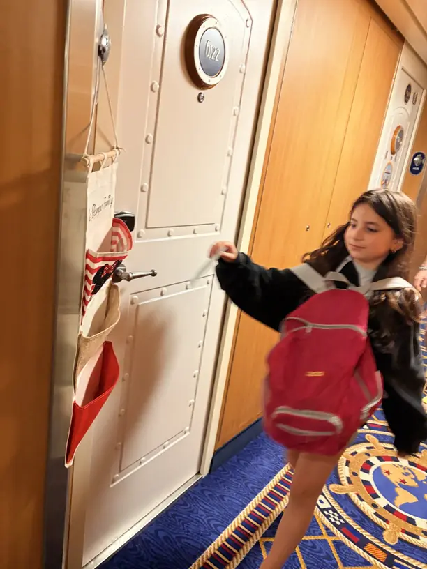 Avilene with her backpack at the stateroom door with a Minnie fish extender hanging beside it