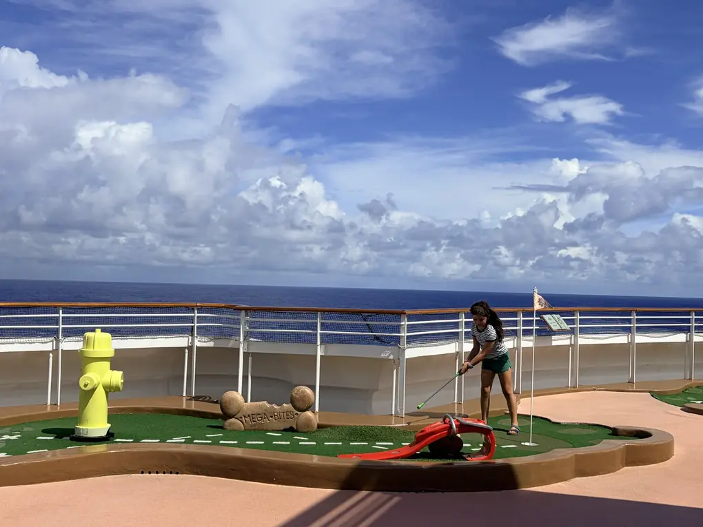 Avilene playing mini golf on the top deck of a Disney cruise with the ocean behind her