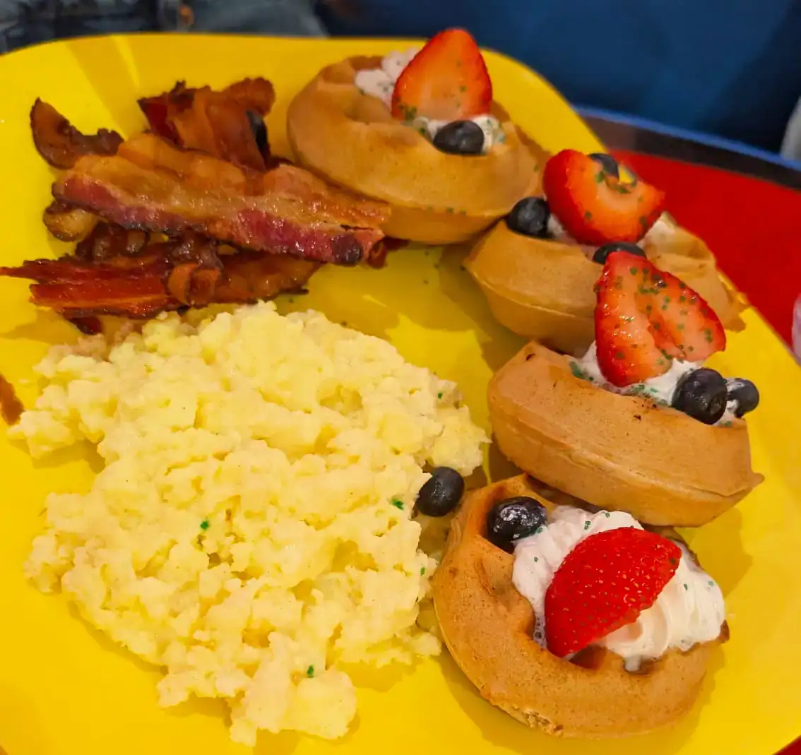 Grinch Breakfast Plate: Mini Waffles, Bacon and Scrambled Eggs - Favorite Grampy Travels Grinch breakfast plate with mini waffles topped with strawberries and blueberries, bacon and scrambled eggs at Universal Orlando