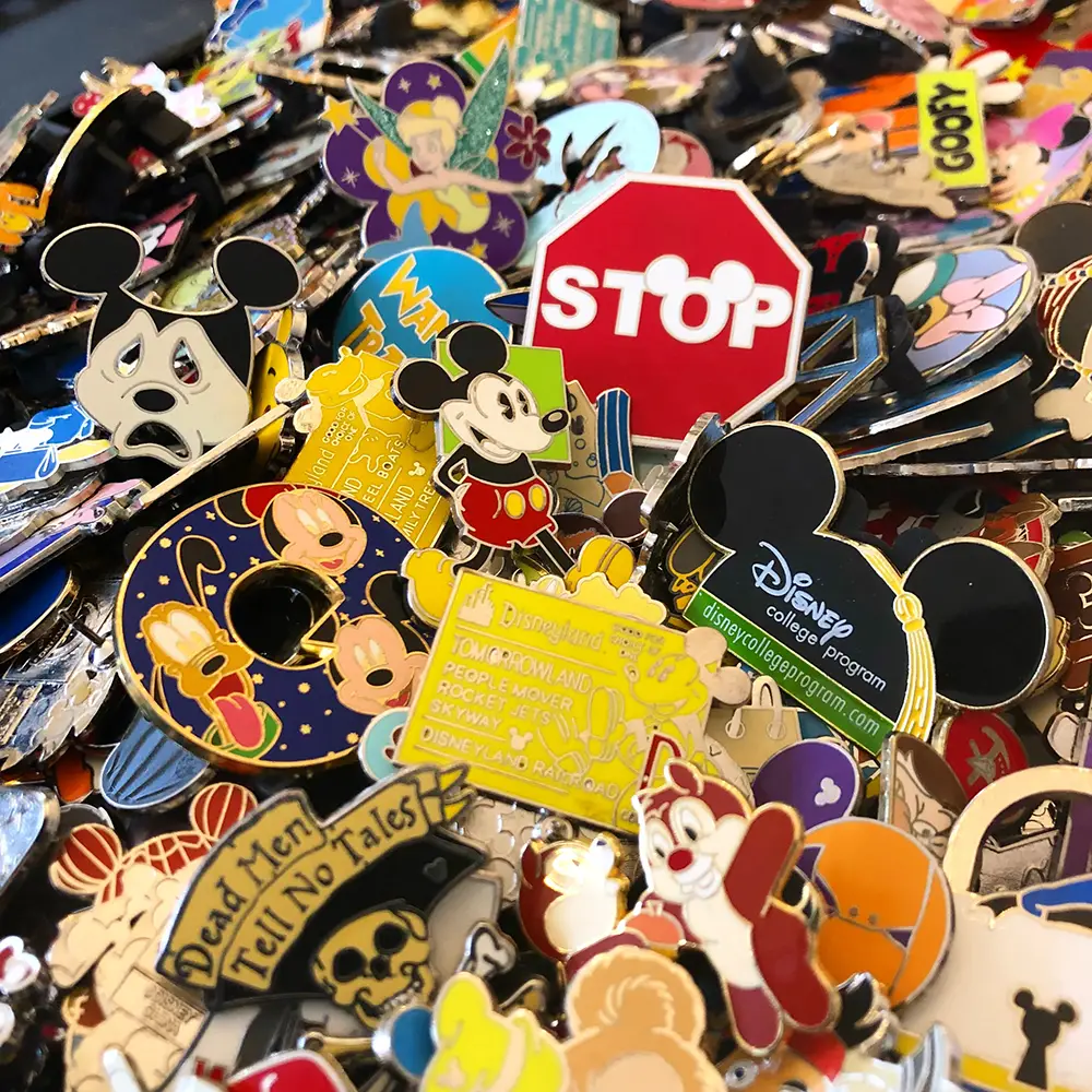 A large pile of Disney-themed enamel pins, including Mickey Mouse, Goofy, Tinker Bell, and a Disney College Program logo, perfect for kids interested in Disney pin trading. - Favorite Grampy Travels