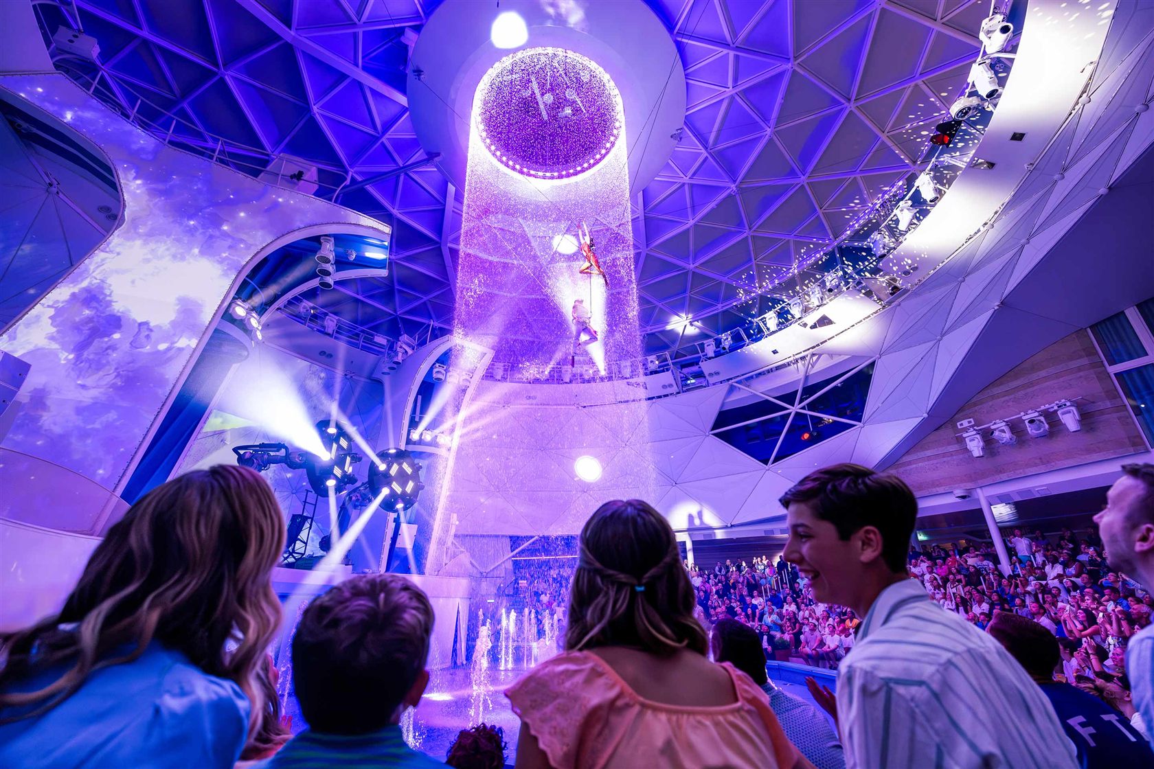 Family watching a water and light show at the AquaTheater inside the AquaDome on Icon of the Seas