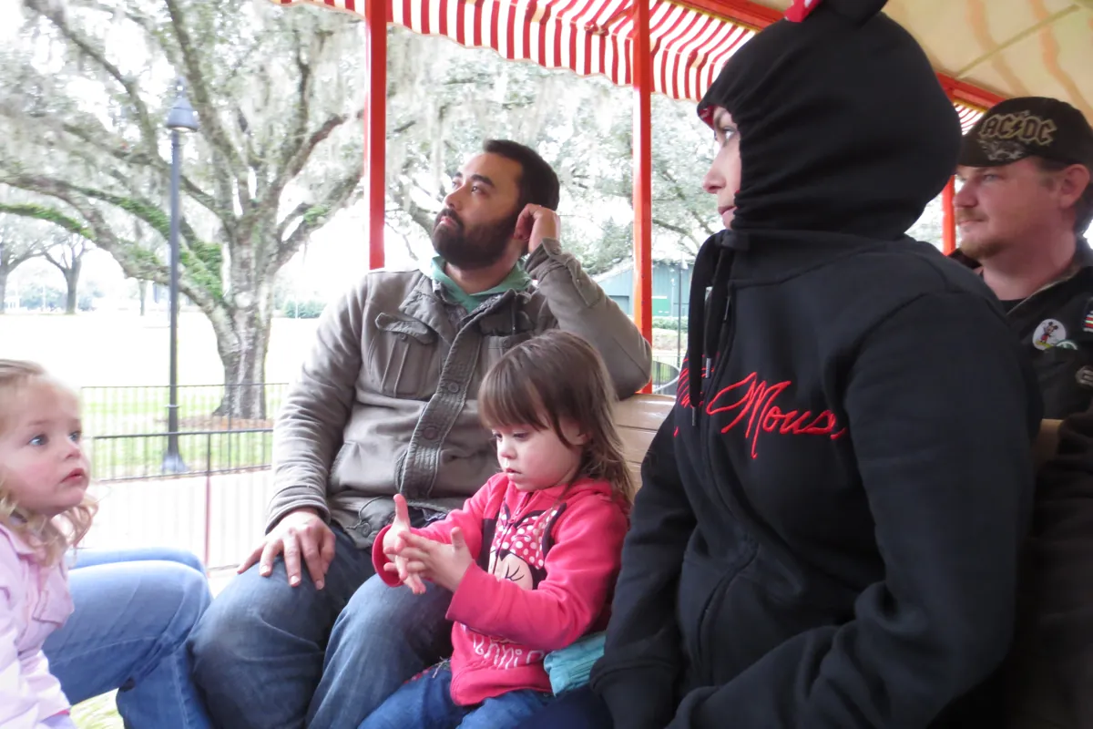 Family with two toddlers taking a rest break on a covered bench at Magic Kingdom on a cool day