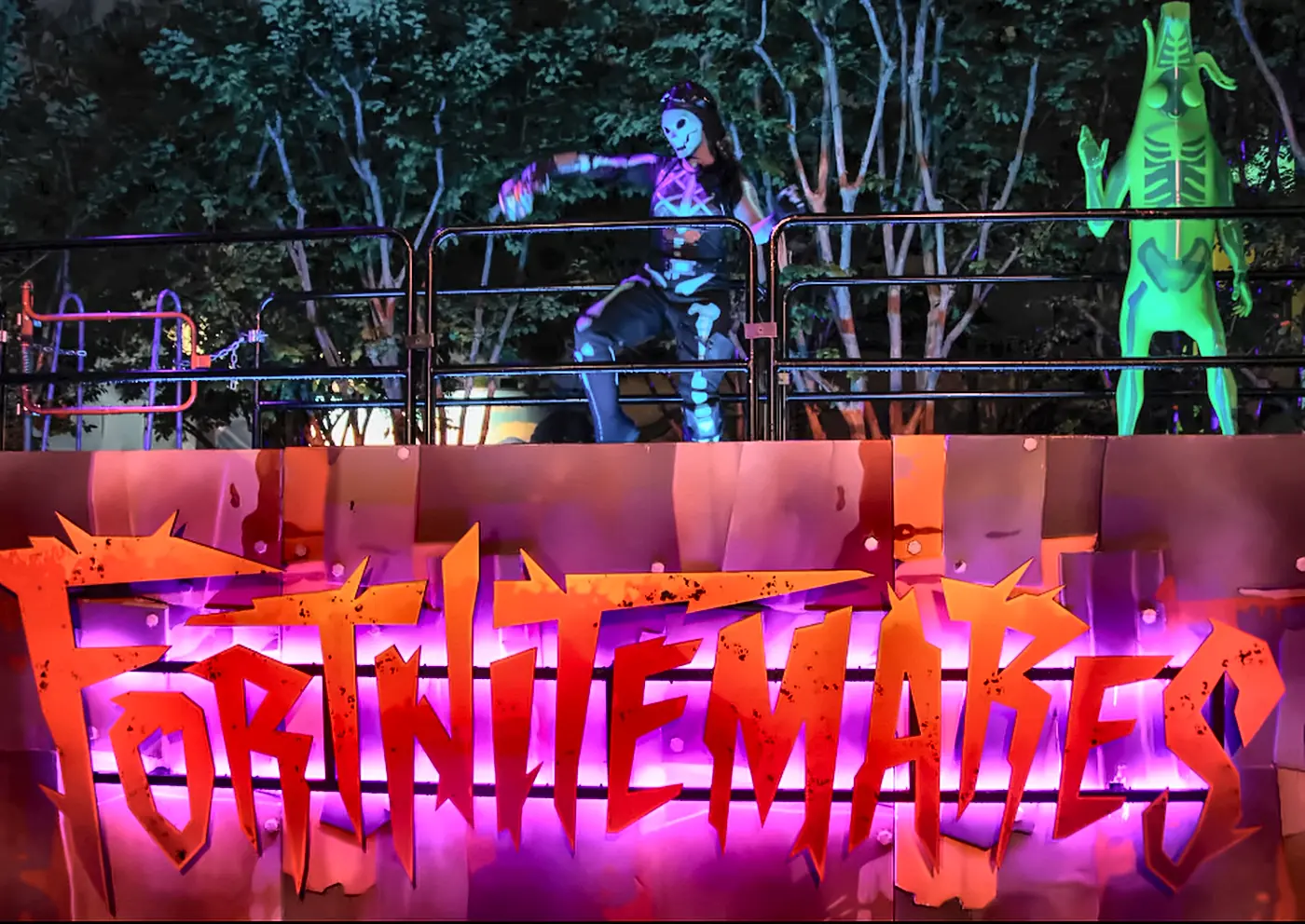 Fortnitemares Scare Zone Sign with Skeleton Scare Actors at Halloween Horror Nights - Favorite Grampy Travels - Favorite Grampy Travels The glowing orange Fortnitemares sign with skeleton-costumed scare actors behind a railing at Halloween Horror Nights.