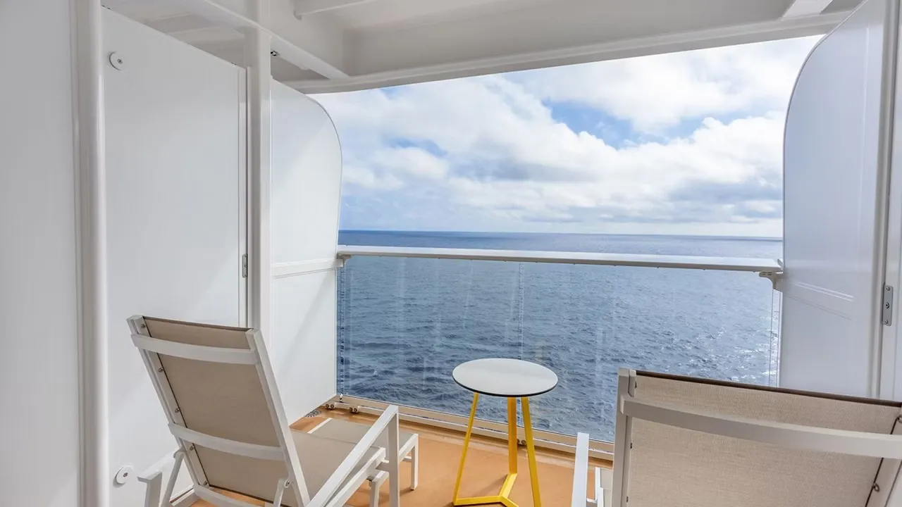 Two balcony chairs and a small table looking out at the ocean from an Icon of the Seas stateroom