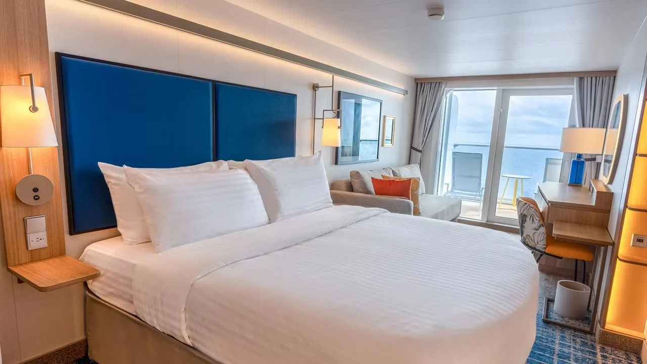 Ocean View stateroom with a queen bed, sofa and glass door to a large balcony on Icon of the Seas