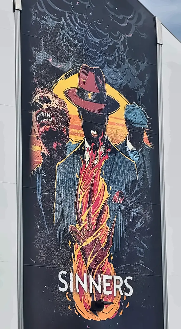 Sinners Haunted House Poster on Facade at Halloween Horror Nights 35 - Favorite Grampy Travels - Favorite Grampy Travels The Sinners haunted house poster on a facade at Halloween Horror Nights 35, showing three figures and a burning hand.