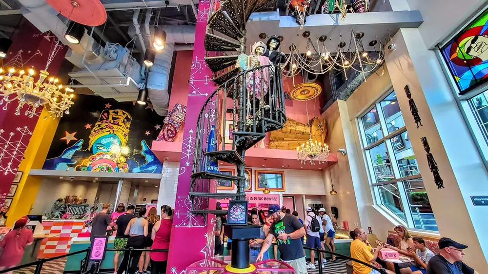 A spiral staircase with two skeletons on the landing stands in a vibrant Universal CityWalk cafe decorated with murals and chandeliers. - Favorite Grampy Travels