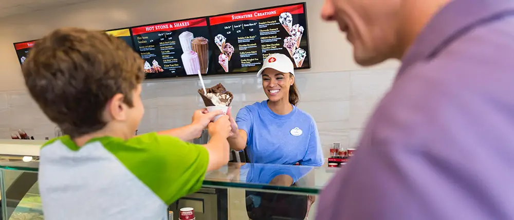 An ice cream shop employee wearing a branded cap and shirt hands a chocolate-dipped cone, one of the best snacks at Universal CityWalk, to a young boy. - Favorite Grampy Travels
