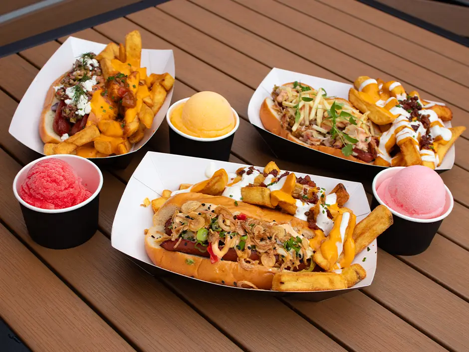 Three hot dogs topped with various ingredients served with fries and colorful sorbet on a wooden table, typical of Universal Orlando dining. - Favorite Grampy Travels