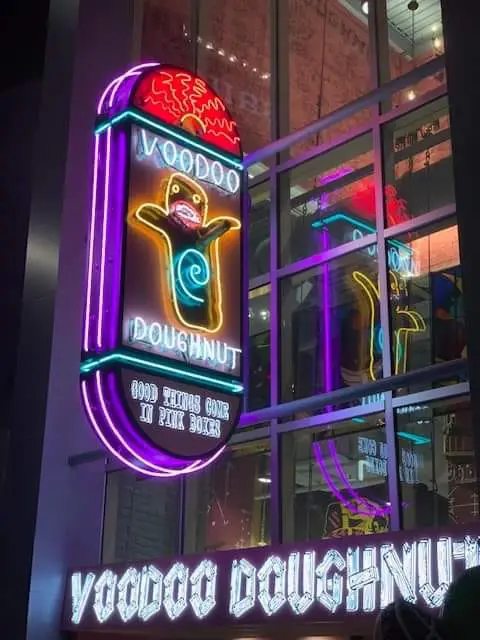 A Voodoo Doughnut neon sign at Universal CityWalk featuring a cartoon voodoo doll above the text Good things come in pink boxes, with a large Voodoo Doughnut sign below. - Favorite Grampy Travels