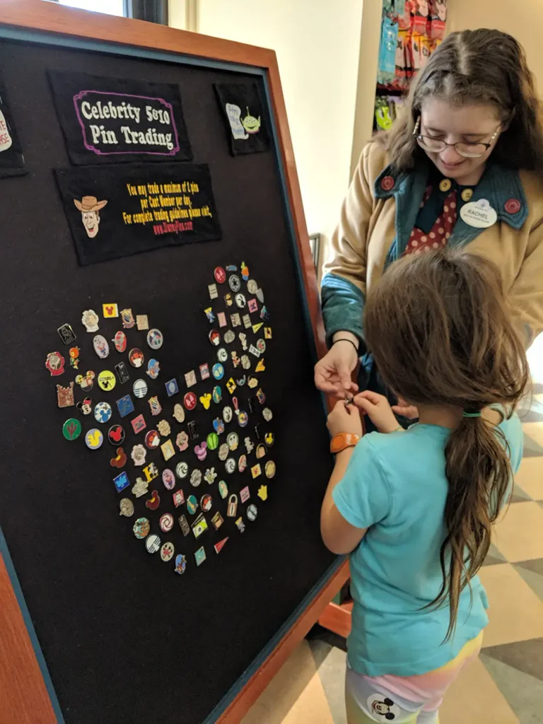 A young girl participates in Disney pin trading as she swaps a pin with a cast member at a board arranged in a heart shape. - Favorite Grampy Travels