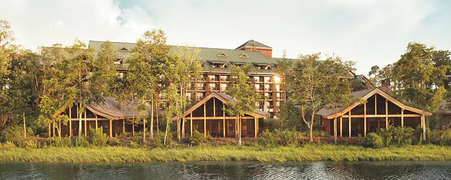 A large Disney Wilderness Lodge wooden lodge with a green metal roof, nestled among trees along a riverbank perfect for a family vacation. - Favorite Grampy Travels