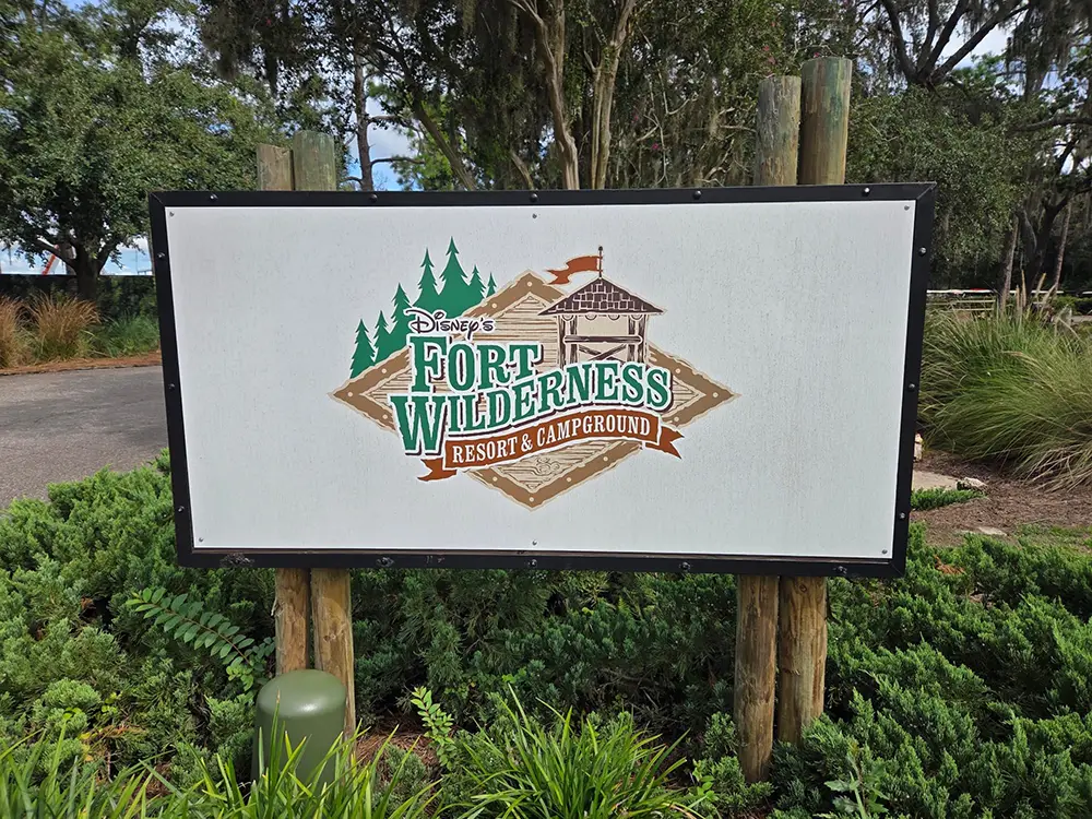 A sign for Disney’s Fort Wilderness Resort & Campground featuring a logo with a wooden fort illustration and pine trees. - Favorite Grampy Travels