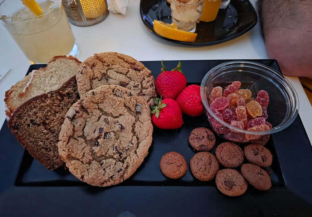 A black rectangular platter holds chocolate chip cookies, quick bread, strawberries, gummy candies, and small chocolate cookies, perfect for snacking while watching Disney fireworks. - Favorite Grampy Travels