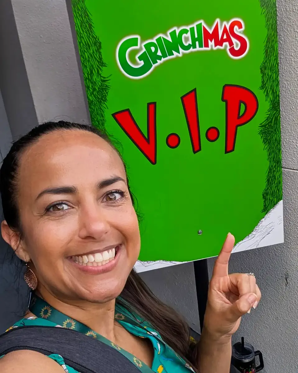 Nikki from Favorite Grampy Travels points to the Grinchmas VIP Tour sign at Universal Orlando