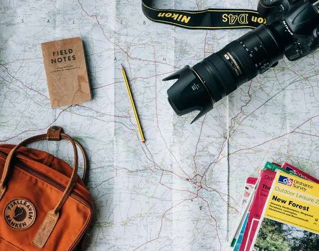 Travel map, camera and backpack laid out on a table while planning a personalized family vacation