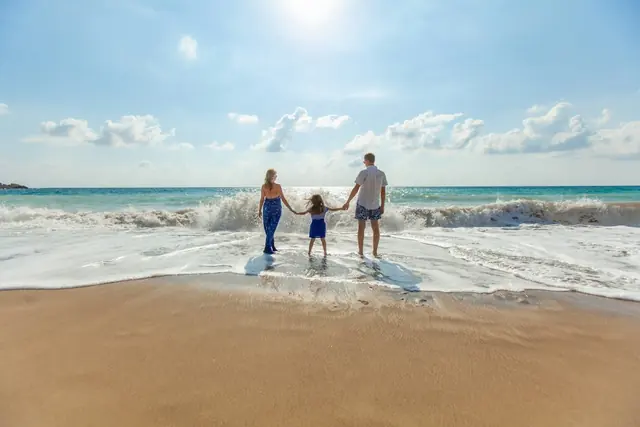 Family holding hands and walking into the ocean surf together on a beach vacation