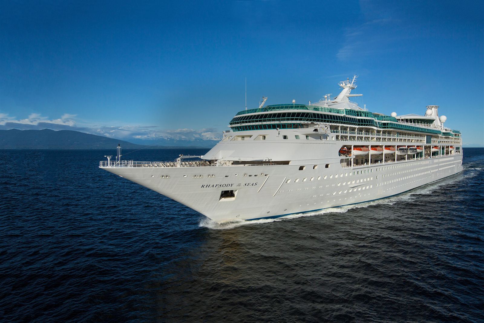 Royal Caribbean's Rhapsody of the Seas, a Vision Class ship, sailing with mountains in the background